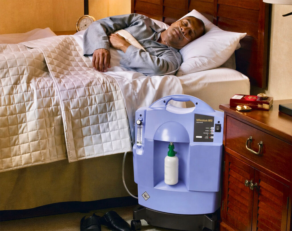 A man is sleeping in bed using a stationary oxygen concentrator.
